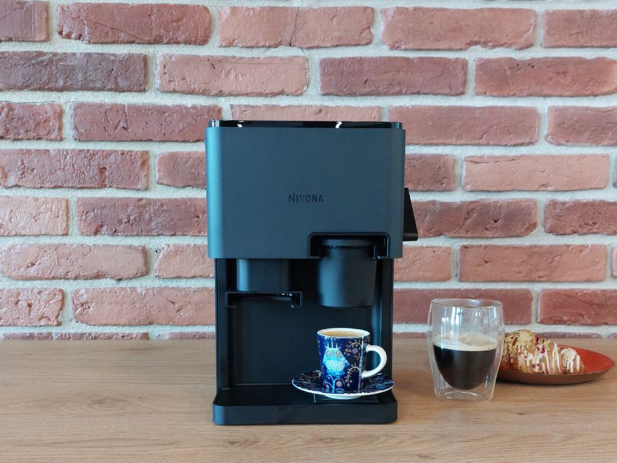 Ekspres automatyczny Nivona Cube z zaparzoną kawą lungo w ładnej filiżance, stoi na tle ceglanej ściany