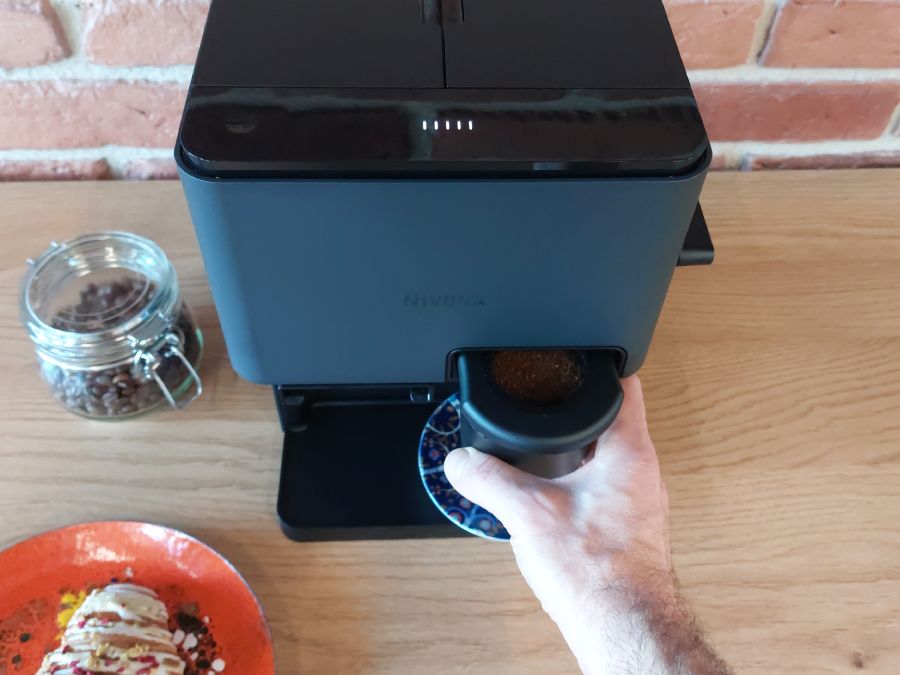 Ktoś wkłada kubek Click Cup ze zmieloną kawą do ekspresu Nivona Cube
